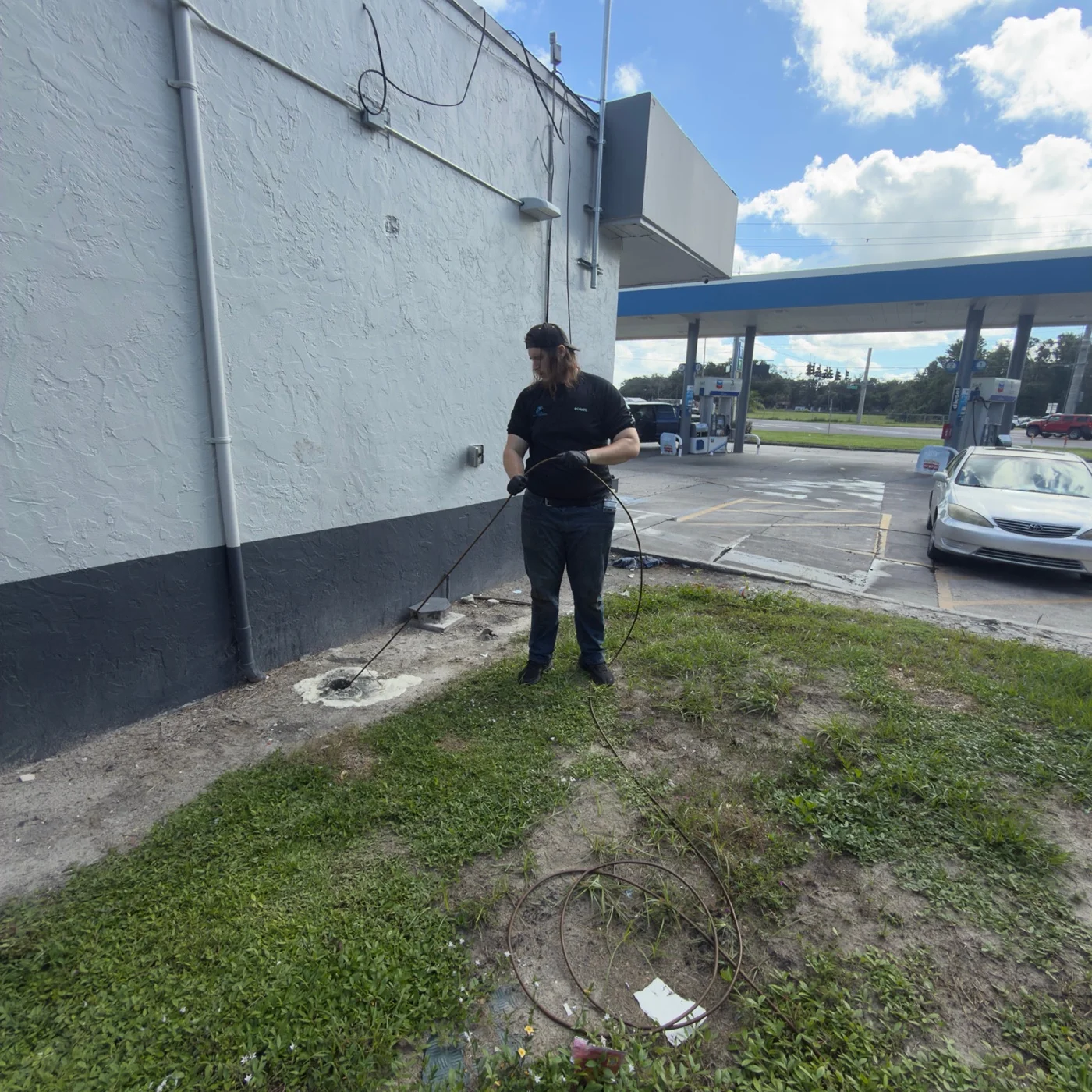 Technician handling a hose at an exterior drain beside a commercial building